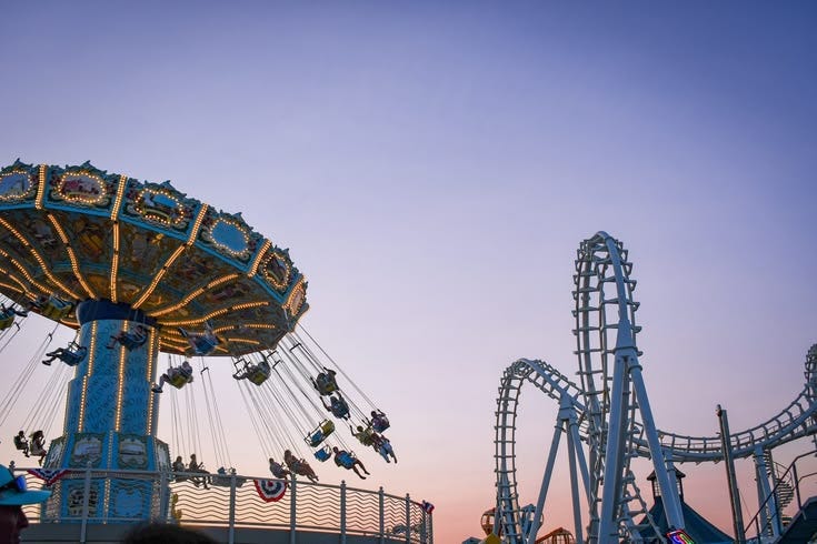 This may contain: people are riding on swings and rides at an amusement park in the evening time as the sun sets