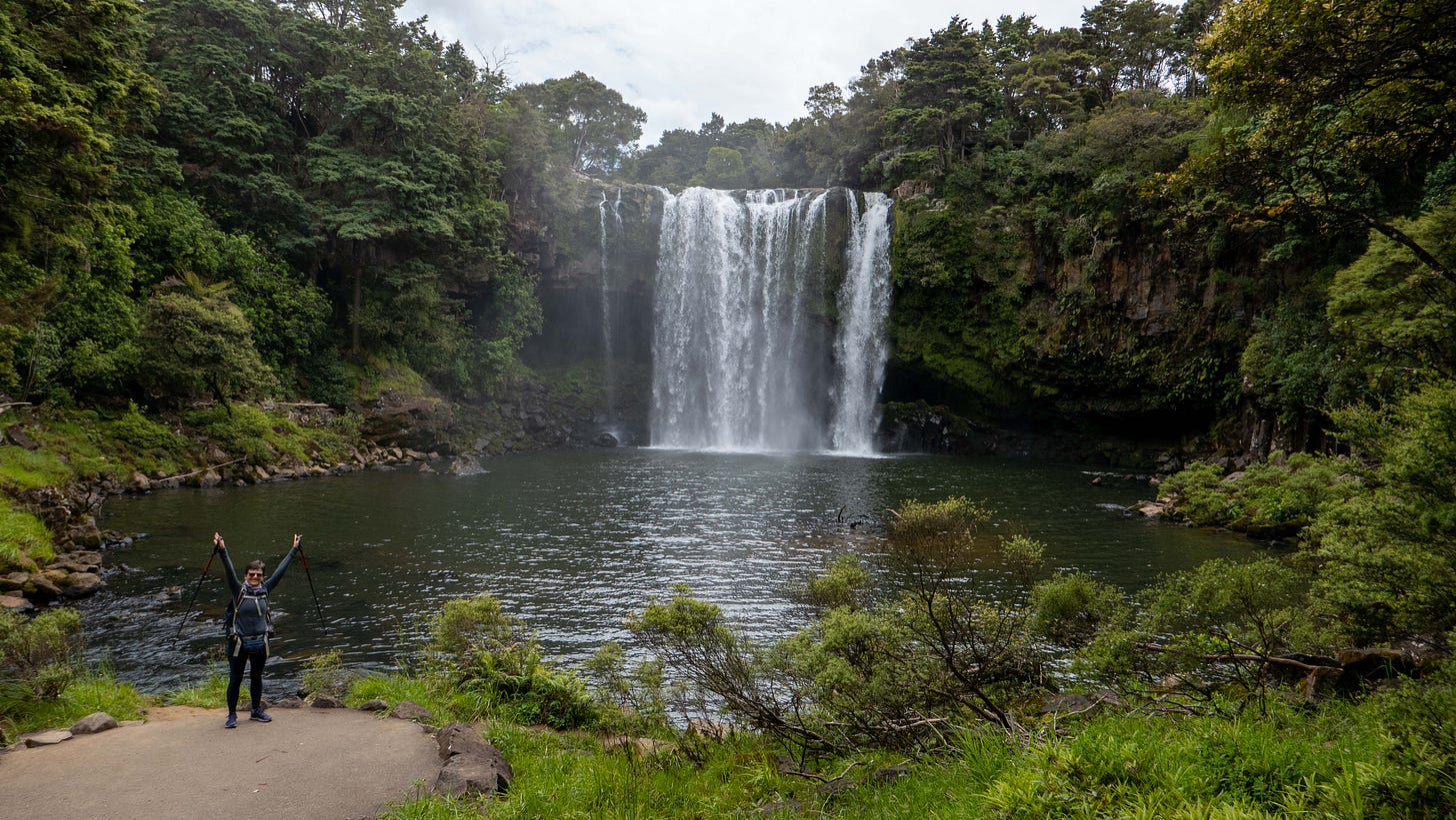Rainbow Waterfalls dropping to a large pool, with Julia standing on a platform at the edge of the pool.