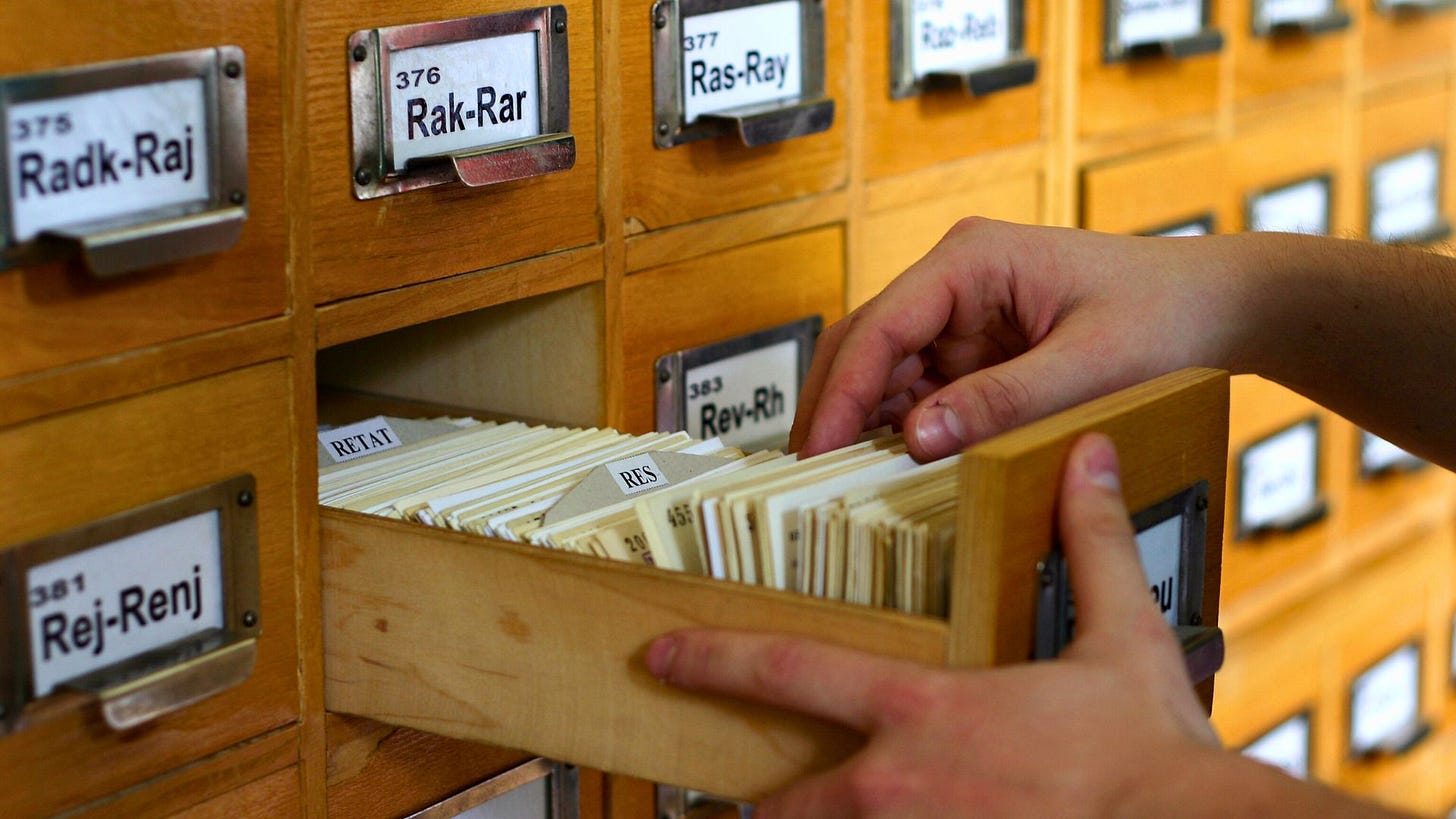 A person pulling out a card catalog drawer filled with index cards.