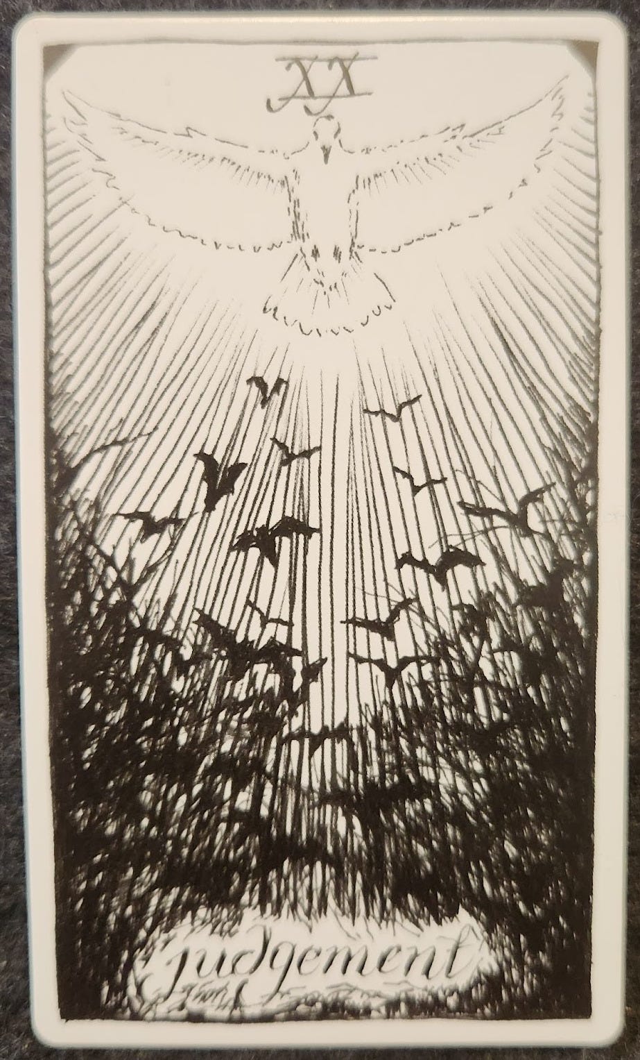 A tarot card labelled XX judgement. A large white bird with its wings spread out wide. Below are a flock of black birds flying towards it. 