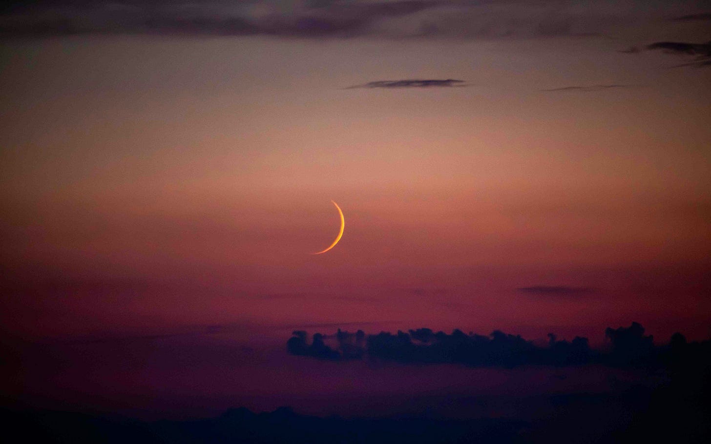 A new moon against a red and grey skyline, signifying change on the horizon.