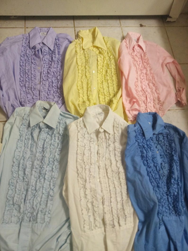 May include: Six ruffled shirts in various pastel colors, including lavender, yellow, pink, light blue, white, and blue. The shirts have a classic button-up design with a ruffled front.
