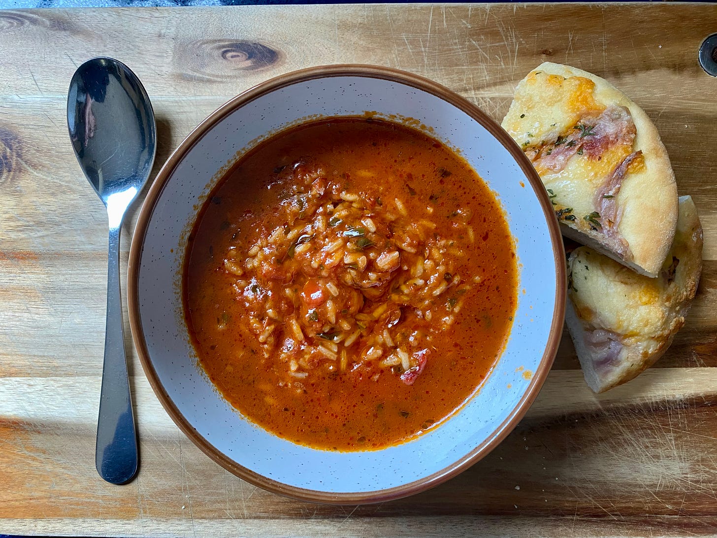 Bowl of tomato and rice soup with a spoon and some bread next to it