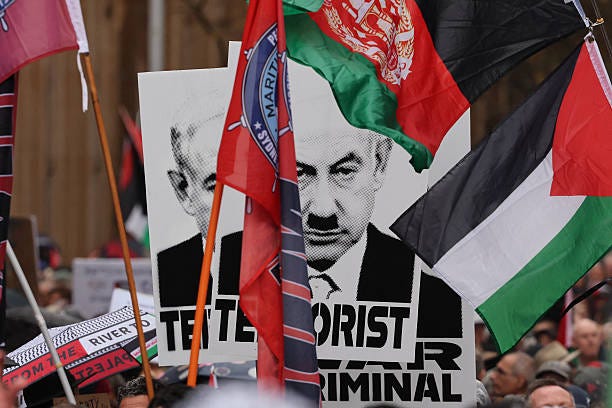 Protesters hold up placards showing a depiction of Israeli Prime Minister Benjamin Netanyahu as Hitler during a pro-Palestinian rally against...