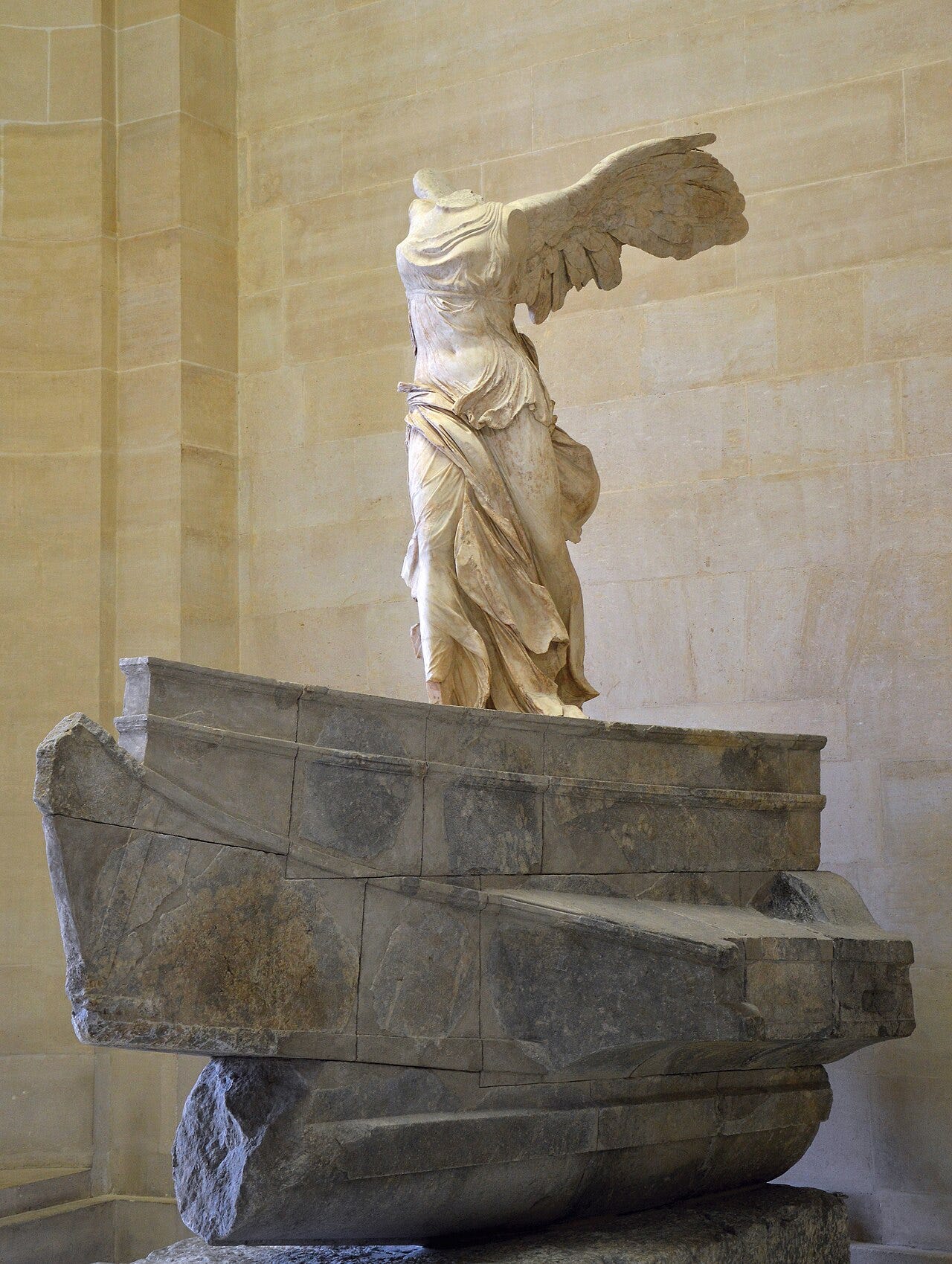 The Winged Victory of Samothrace at the top of the Daru staircase in the Louvre, wings spread on the prow of a stone ship