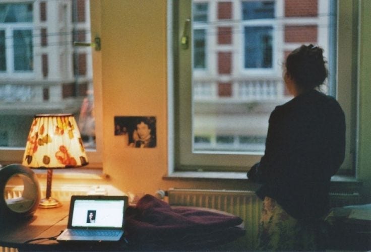This may contain: a woman sitting in front of a window with a laptop computer on her desk next to a lamp