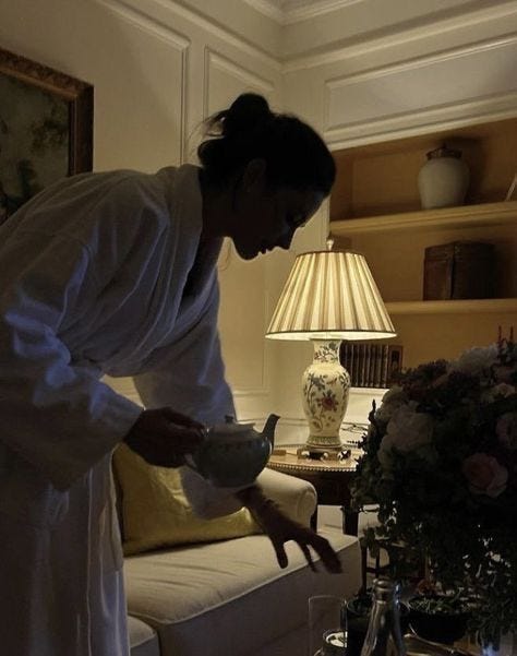 This may contain: a woman in white robe holding a bowl near a table with vases on it