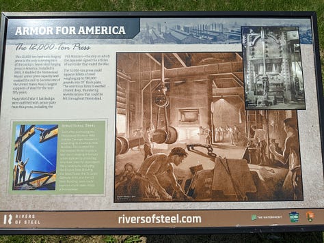 The remains of a massive 12,000 ton press now a rusting frame standing outdoors behind a chain-link fence on a bright blue day.