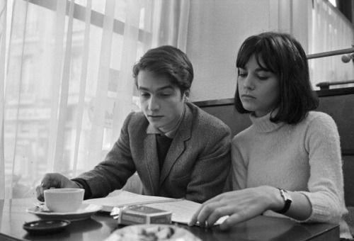 This may contain: a man and woman sitting at a table in front of a book with a cup of coffee