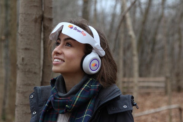 photo of a woman in a forest wearing a BrainTap headset and smiling photo of a woman in a forest wearing a BrainTap headset and smiling