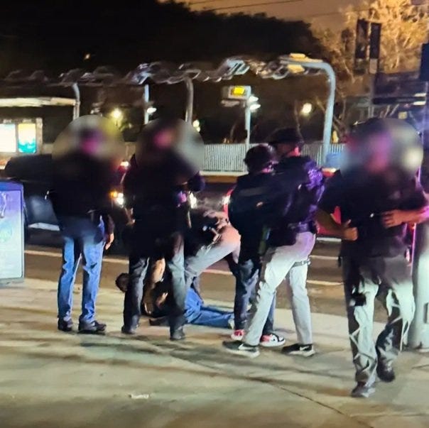 Police officers apprehending a suspect on a city street at night, with bystanders observing the scene. Police officers apprehending a suspect on a city street at night, with bystanders observing the scene.