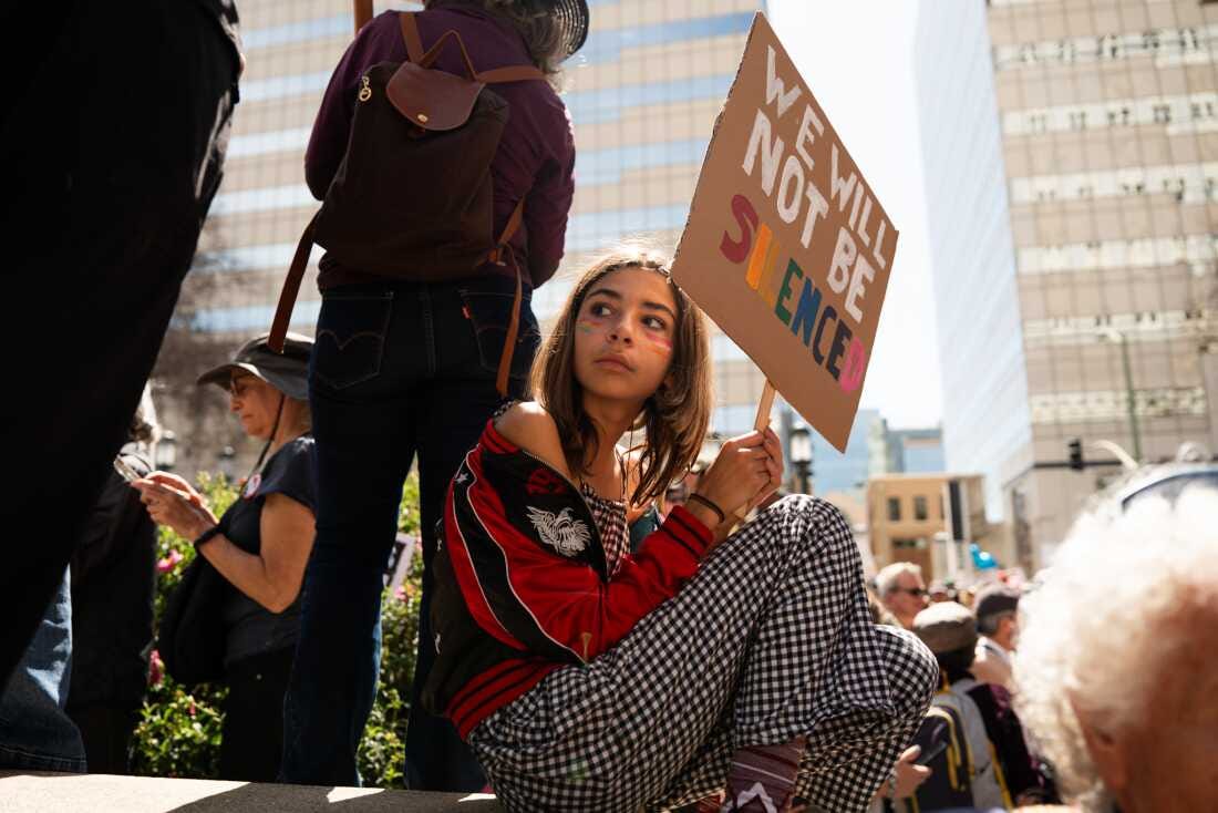 A protester sits with a sign saying “we will not be silenced”