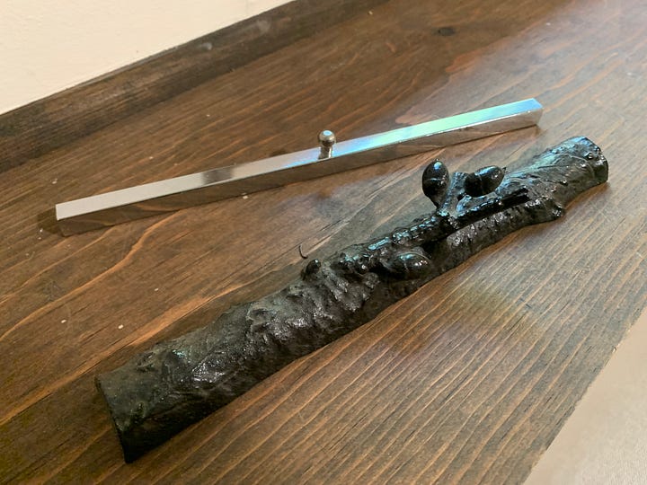 Left, Two long narrow paperweights, one a stainless steel bar with a knob handle and one in the shape of a branch with a smaller branch coming off it as a handle; right, four antique irons made of cast iron, one in miniature