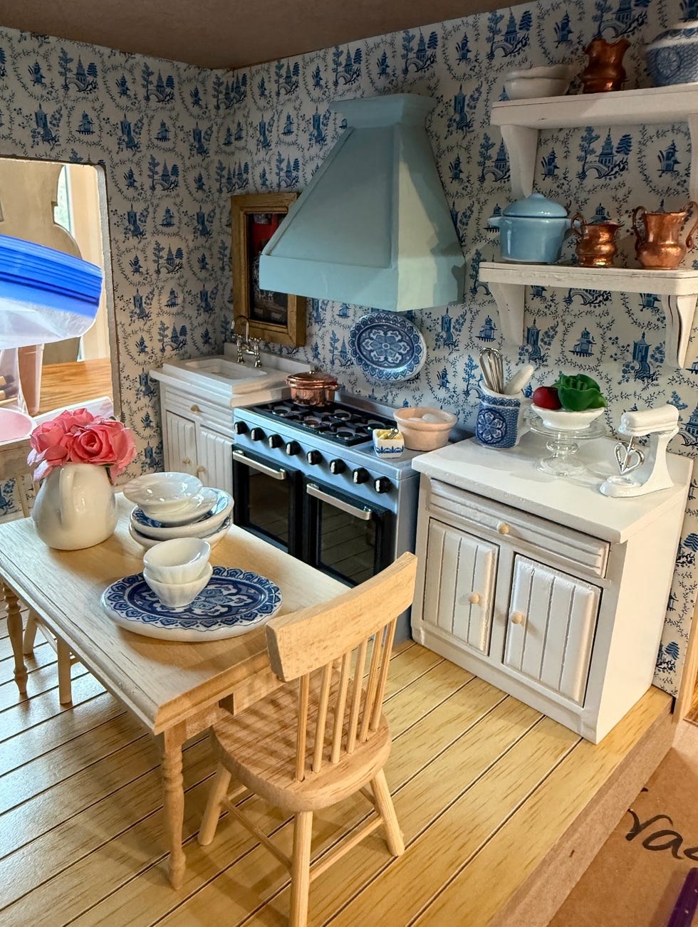 A detailed miniature kitchen scene with a wooden dining table, dishes, and decorative items on shelves. A detailed miniature kitchen scene with a wooden dining table, dishes, and decorative items on shelves.