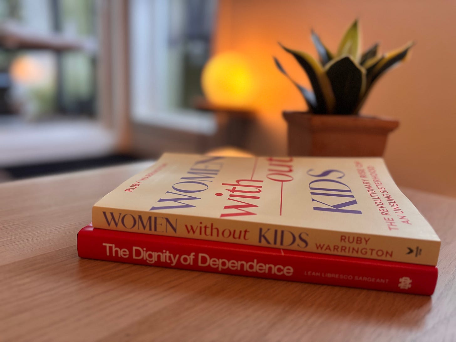 Two books, "Women Without Kids" and "Dignity of Dependence" sit on my coffee table. A desert plant of some sort is behind them.