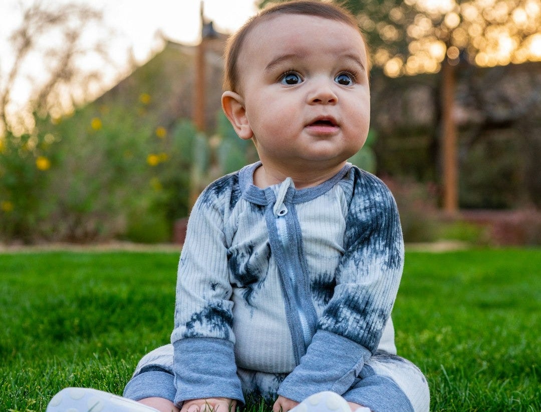 baby in gray sweater sitting on green grass field during daytime