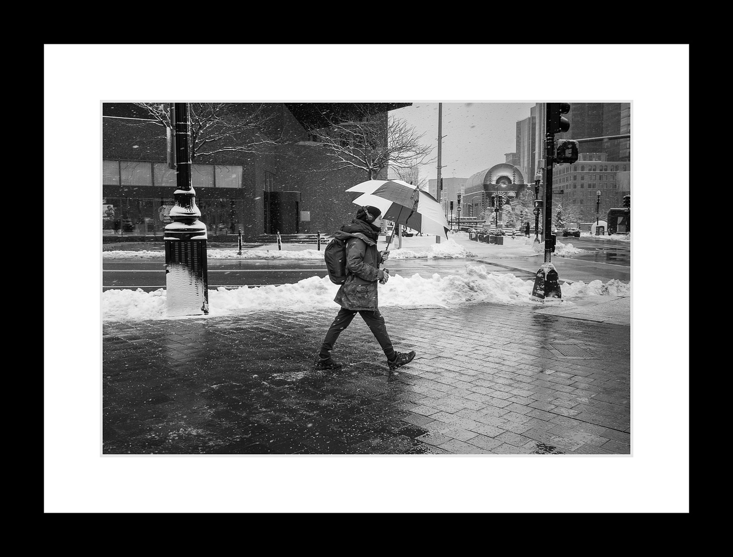 Person walking under umbrella through icy Boston street in winter storm, with reflections on wet pavement.