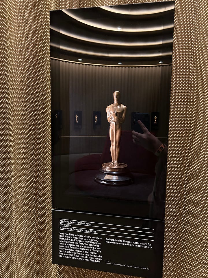 Viola Davis on a screen, costumes on mannequins, Marlee Matlin accepting her Oscar, an Oscar in a case, and photos of the Black Panthers from a documentary.