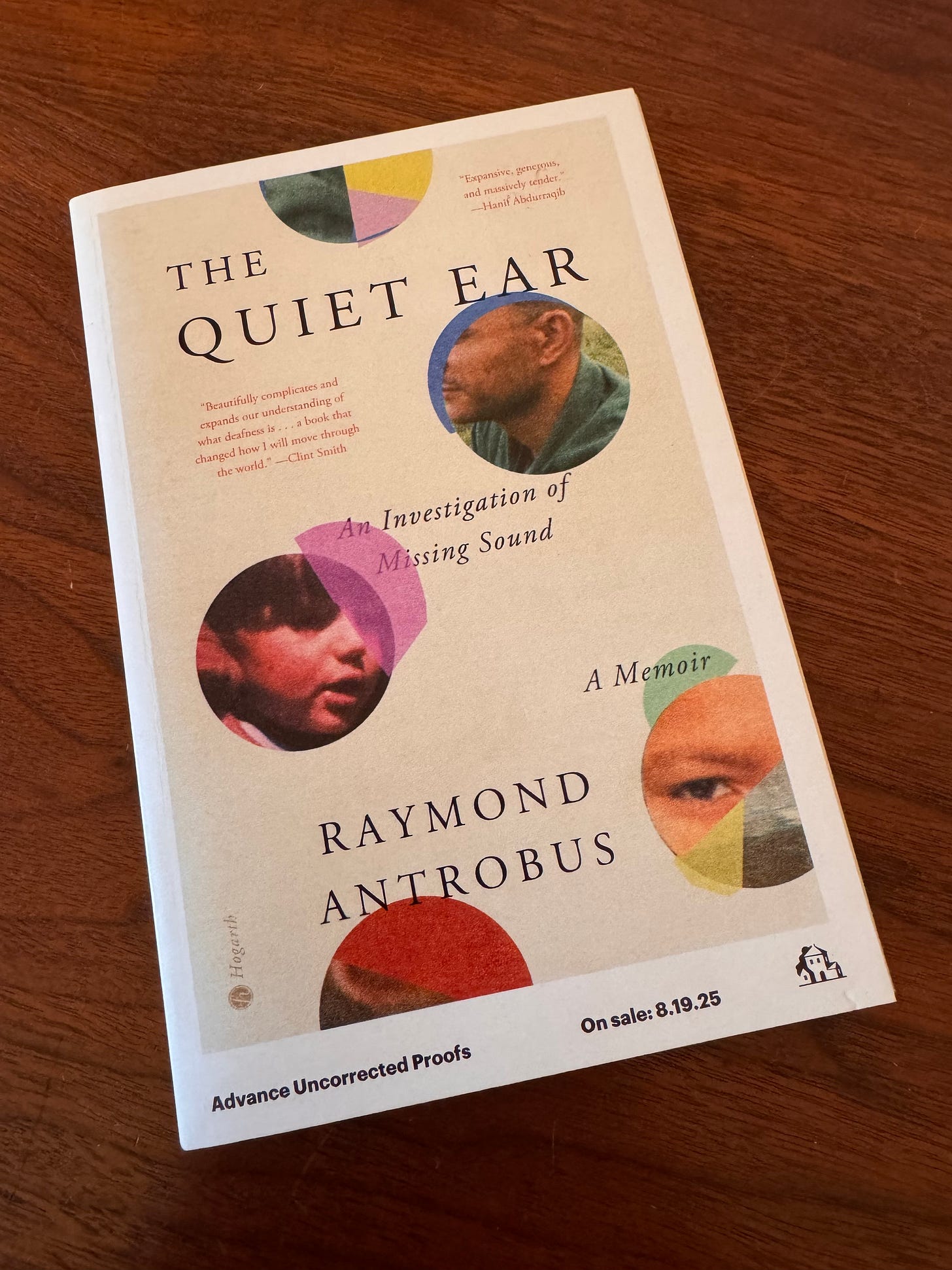 Advance copy of Raymond Antrobus's memoir The Quiet Ear sits on a wooden desk. The cover features the title, alongside assorted circles with close-ups of Antrobus's childhood face, ear, and eyes.