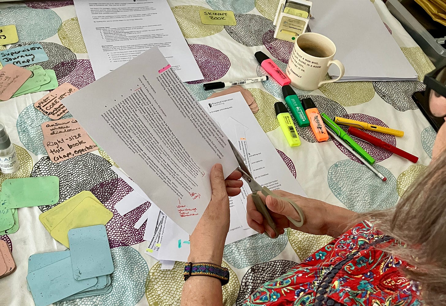 Close-up of table with whiteboard cards and Claire trimming pages to organise book ideas. Close-up of table with whiteboard cards and Claire trimming pages to organise book ideas.