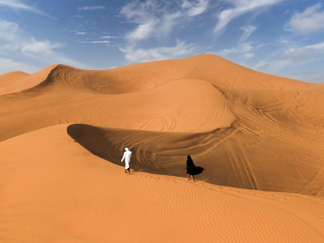 man in black jacket and white pants standing on brown sand under blue sky during daytime
