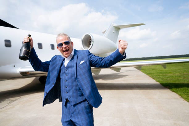 Cheerful male traveller holding champagne bottle and punching the air by private jet Caucasian man in mid 50s wearing three-piece suit, standing on airport tarmac, and celebrating a memorable flight on private jet. rich influencer plane stock pictures, royalty-free photos & images