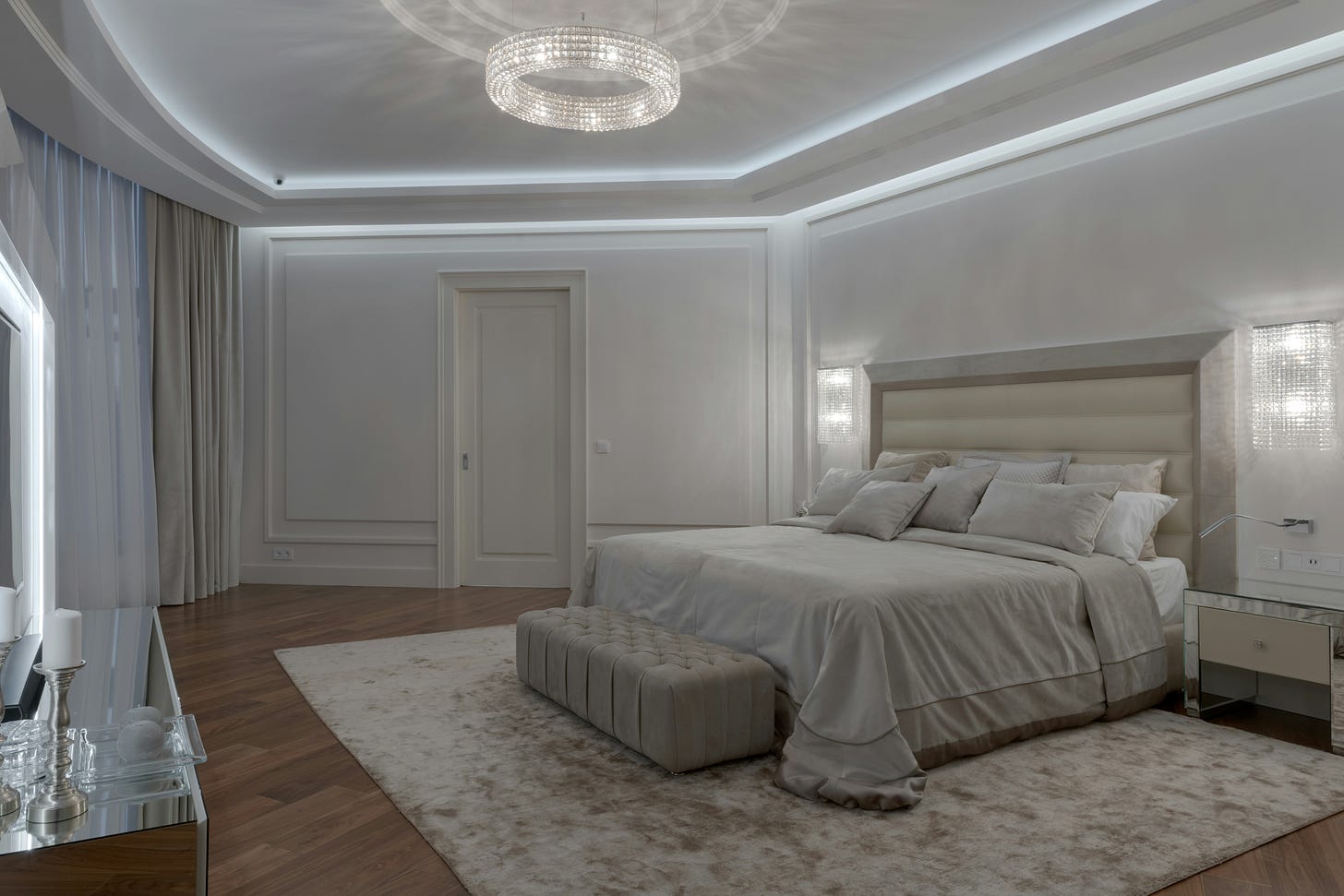 A bedroom with a vanity on the left. The bed has white sheets and the walls are white. 