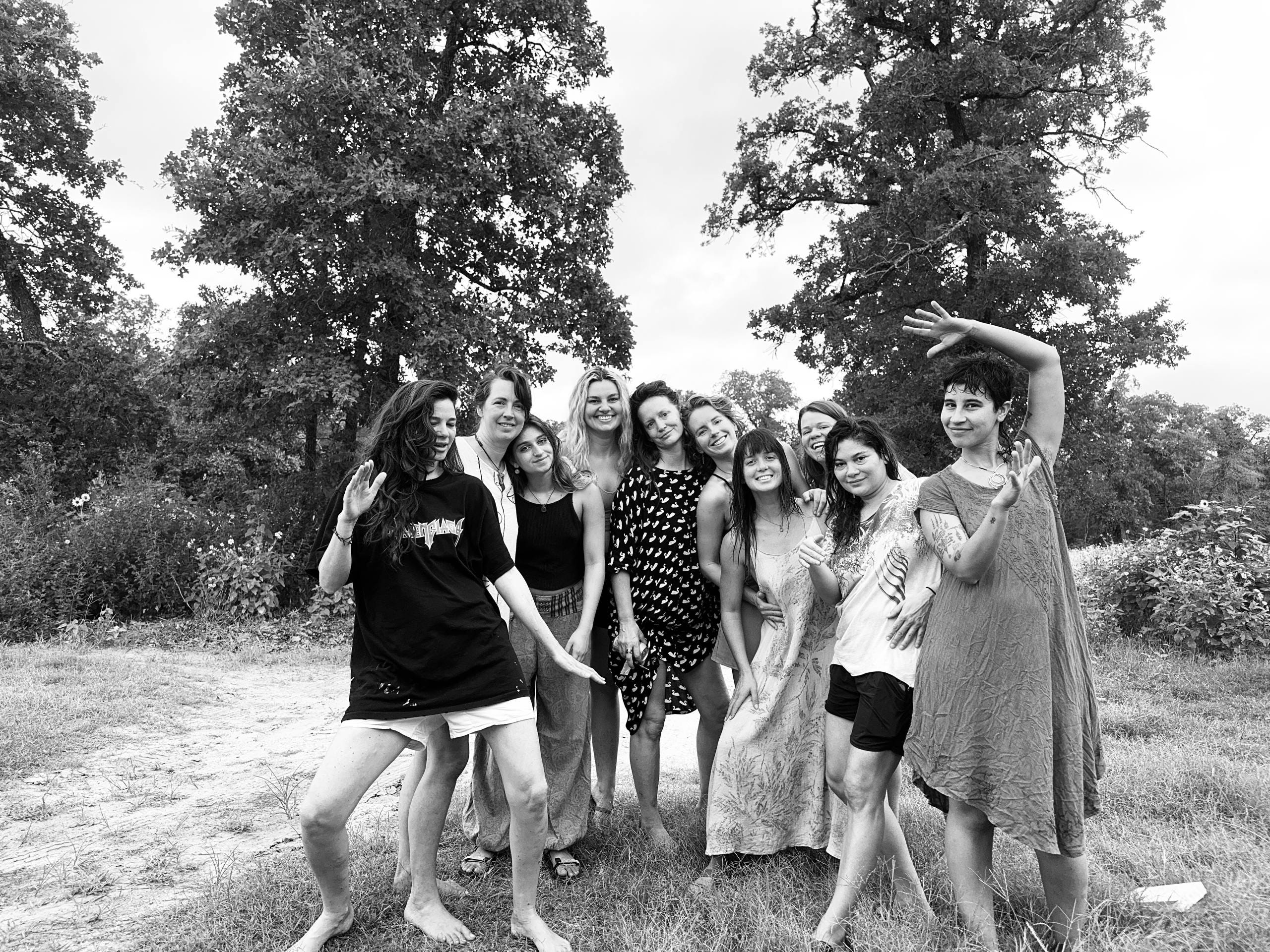 Black and white photograph of ten women standing close together under oak trees, several laughing