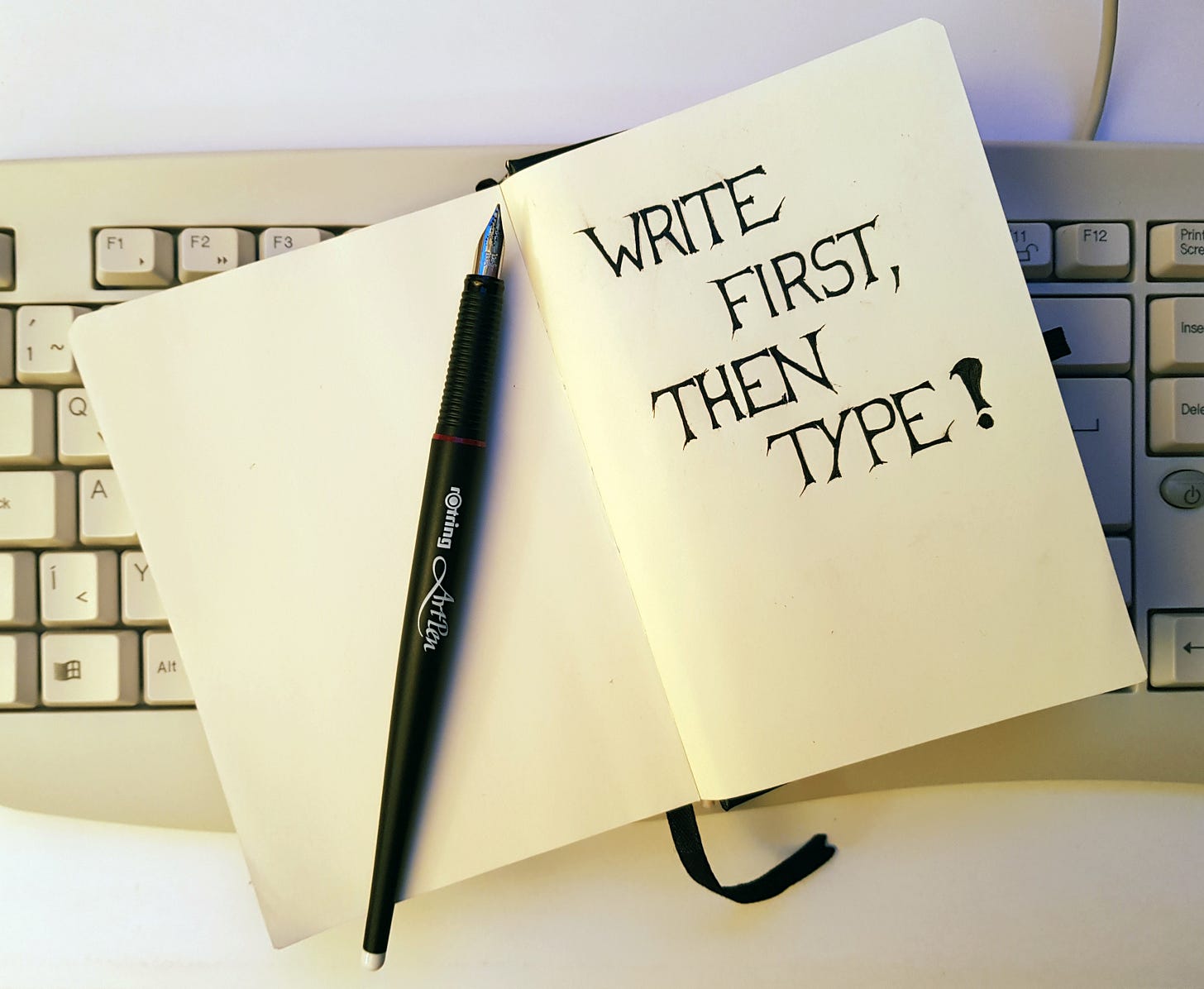 Egy fehér színű számítógép billentyűzeten egy papír notebook van kinyitva. A szerző, József Manhertz mindig ezt használja jegyzetelésre. A jobb oldalra nagy fekete betűkkel az van írva, hogy "Write first, then type!". A bal lapon pedig egy fekete Rotring ArtPen tintatoll van kupak nélkül.