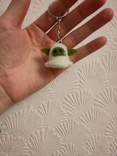 9 pictures of different fiber arts projects including a knit tapestry that says "Protect Trans Youth, a crochet tapestry of a wee ghost, a crochet blanket, a table runner, needle felted keychains, a butterfly cardigan for a little kid, and a blue and white striped cardigan for an adult.