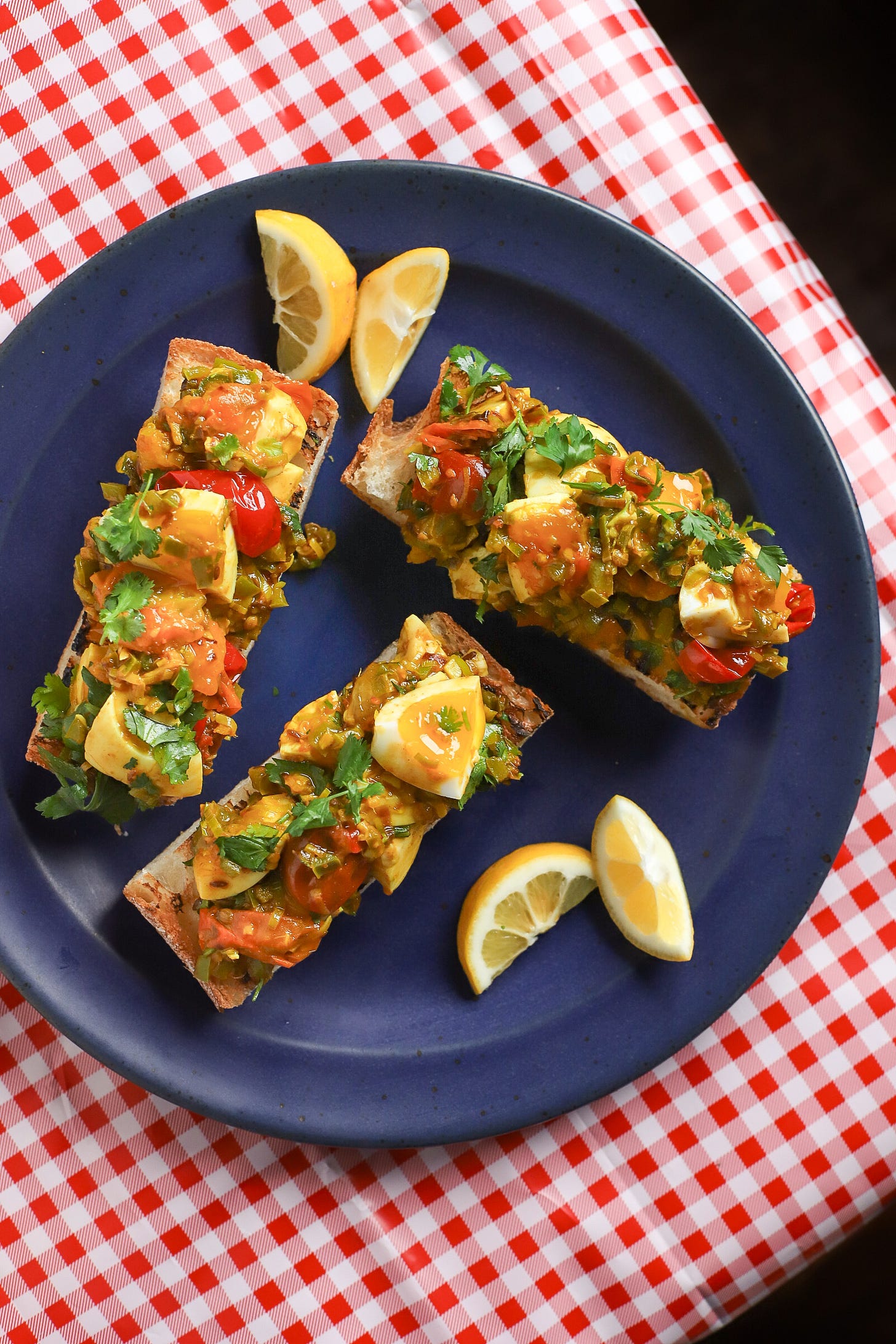 Three toasts with spiced jammy eggs on blue plate and red-checkered tablecloth