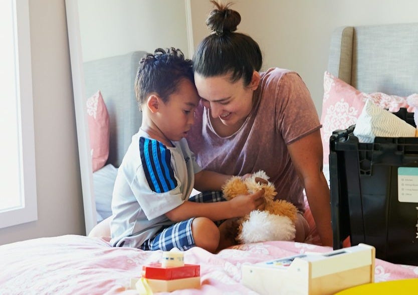 woman in pink long sleeve shirt sitting on bed beside girl in white and blue shirt woman in pink long sleeve shirt sitting on bed beside girl in white and blue shirt