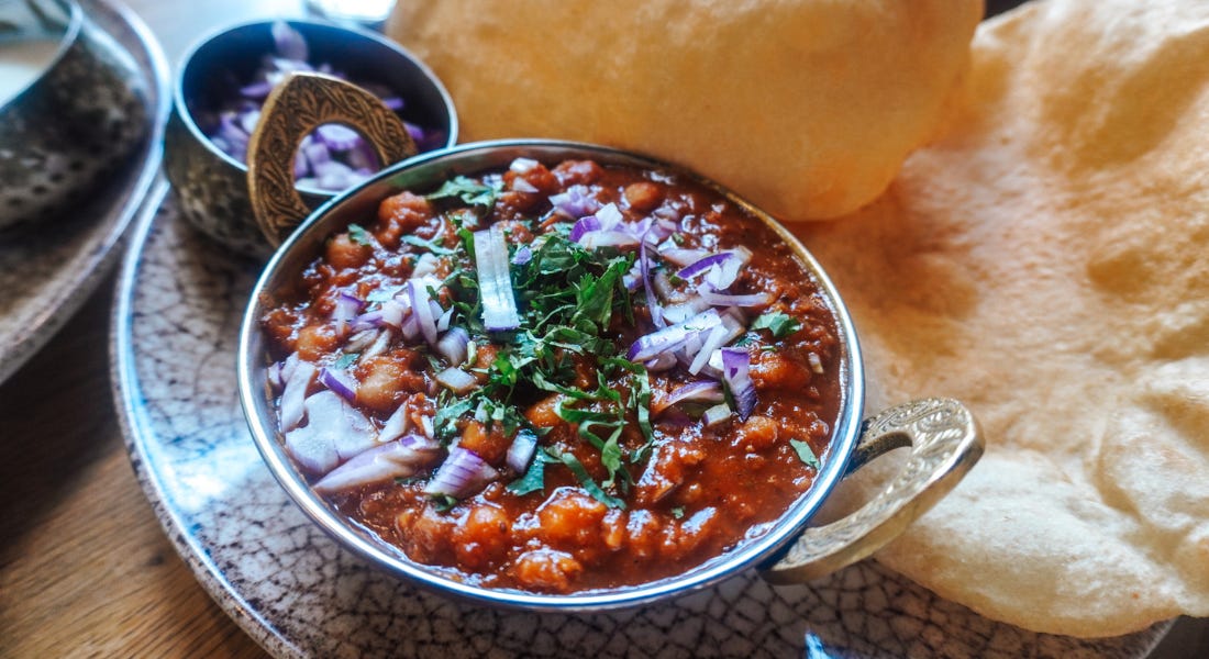 A bowl of chickpea curry on a plate with bread next to it
