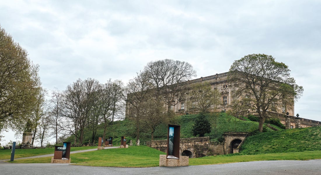 A brown stone castle on top of a hill with a lawn and trees around it A brown stone castle on top of a hill with a lawn and trees around it
