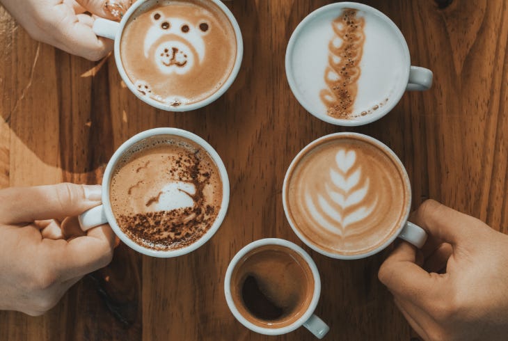 a group of hands holding coffee mugs on a wooden table