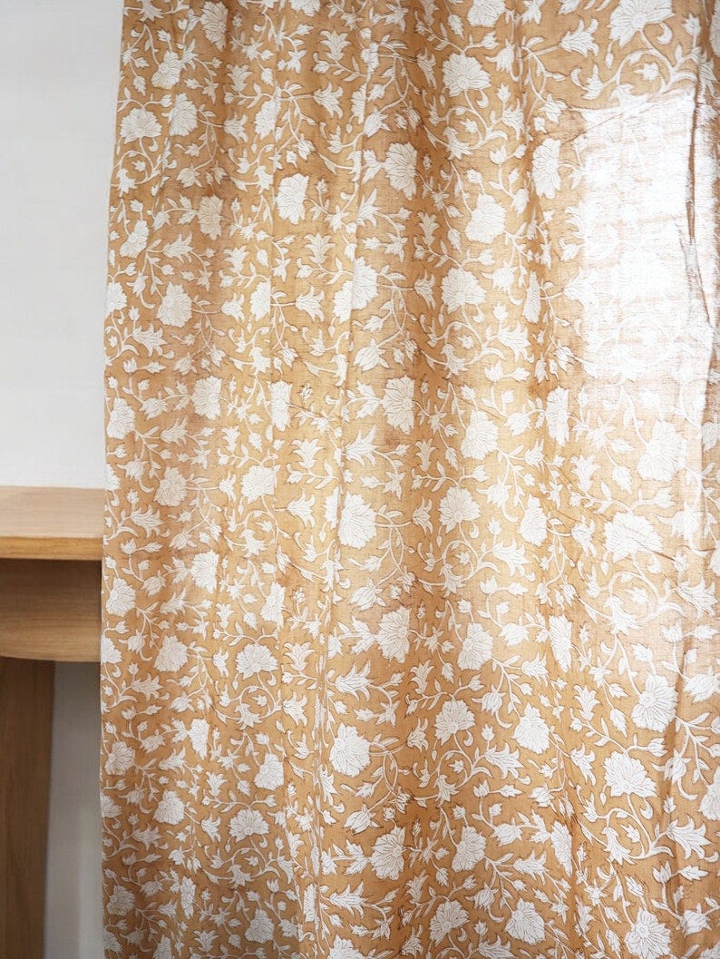 May include: A sheer curtain with a white floral pattern on a light brown background.