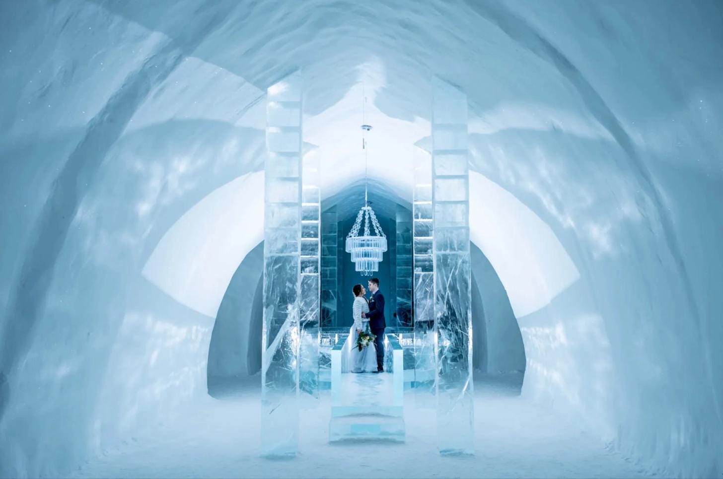 Two guests relaxing inside ICEHOTEL surrounded by ice sculptures and frozen architecture.