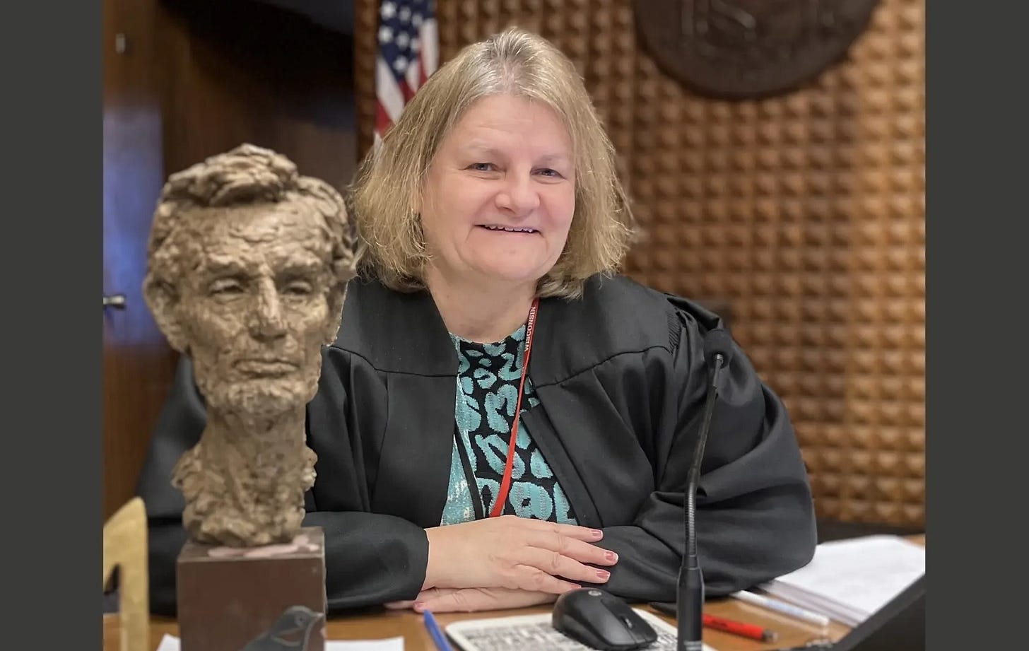 Photo of Judge Hannah Dugan in a courtroom, wearing her black robe, with a bust of Abraham Lincoln on her desk