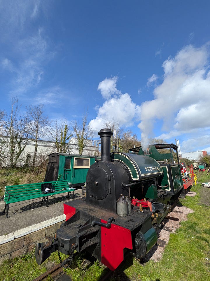 A small green steam train and some wagons, with blue sky