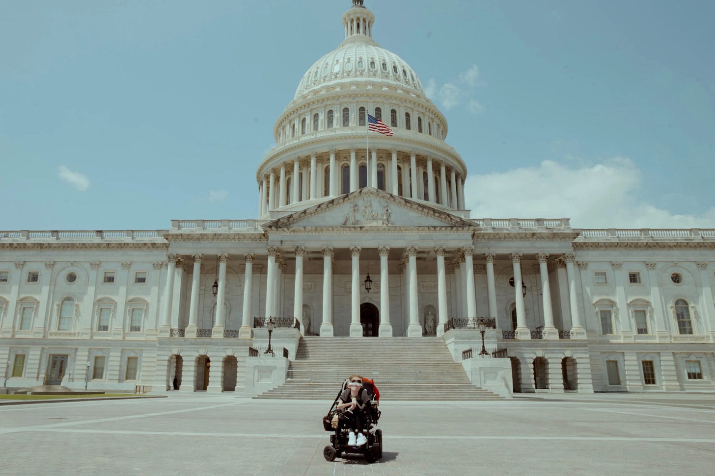 A disabled man in a powerchair outside the Capitol building in Washington DC. There is no one else in the wideshot, making the man look small relative to the huge building and its stairs. A disabled man in a powerchair outside the Capitol building in Washington DC. There is no one else in the wideshot, making the man look small relative to the huge building and its stairs.