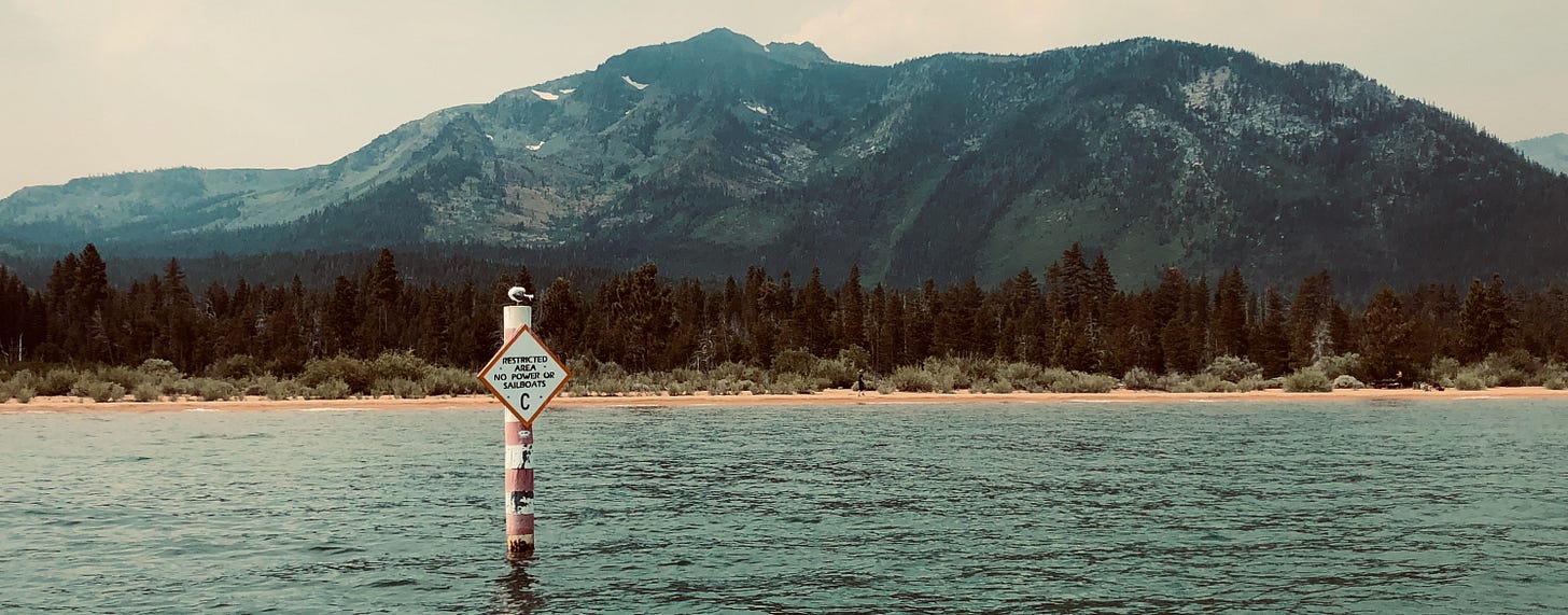 A water safety sign in South Lake Tahoe marking a restricted area with the text ‘No Power or Sailboats.’ The sign is mounted on a post in the water, with a scenic backdrop of mountains, pine forests, and a sandy shoreline. This area between Pope Beach and Baldwin Beach is a designated swimming zone, offering a safer environment for swimmers. A water safety sign in South Lake Tahoe marking a restricted area with the text ‘No Power or Sailboats.’ The sign is mounted on a post in the water, with a scenic backdrop of mountains, pine forests, and a sandy shoreline. This area between Pope Beach and Baldwin Beach is a designated swimming zone, offering a safer environment for swimmers.
