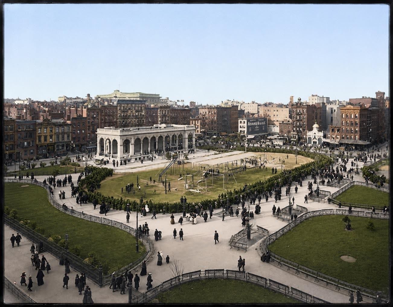 A large city park with curved walking paths, inviting playgrounds, and a central pavilion hosts crowds of people on a clear day. Surrounding buildings rise in the background. A large city park with curved walking paths, inviting playgrounds, and a central pavilion hosts crowds of people on a clear day. Surrounding buildings rise in the background.