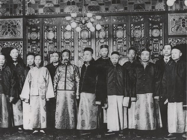 Black and white photograph. Thirteen men in traditional Chinese dress. Black and white photograph. Thirteen men in traditional Chinese dress.