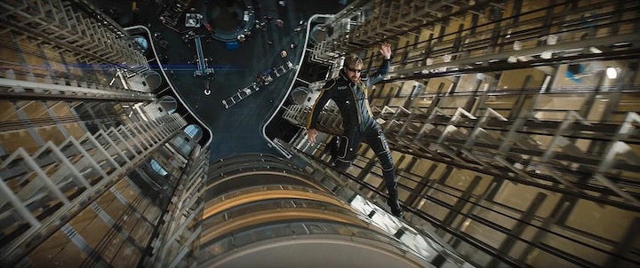 Ryan Gosling mid-fall inside a towering glass-and-steel structure, captured from a dramatic overhead angle that emphasizes the stunt scale.