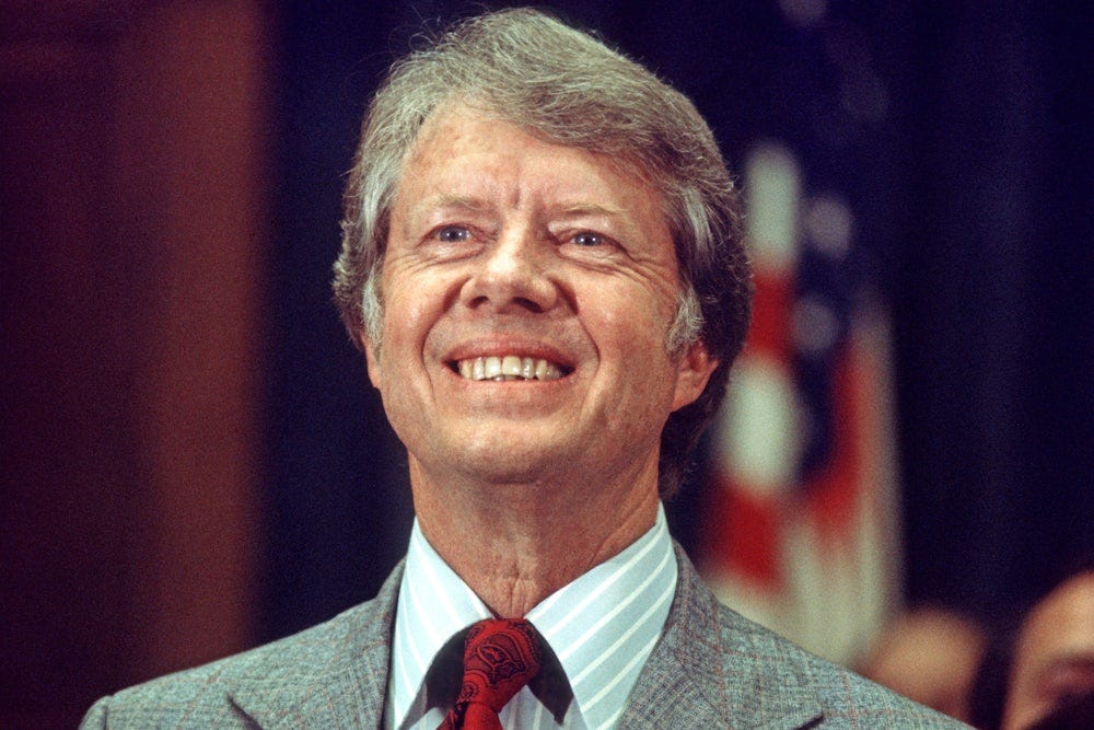 Jimmy Carter, running for reelection, smiles a big toothy grin in front of an American flag. 