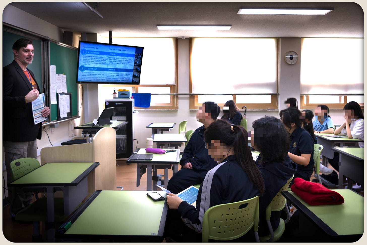 Classroom scene at a South Korean high school: a teacher speaks while students listen, with a slide on screen showing the ‘4Rs’ framework for a labyrinth walk.
