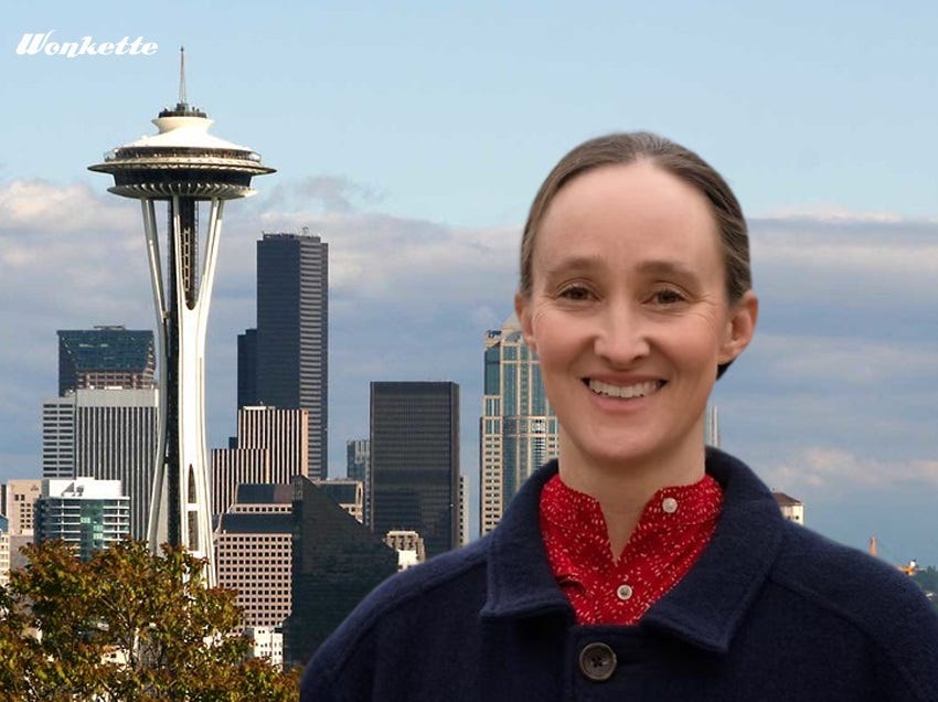 A photoshopped image in which a smiling Katie Wilson, in blue cloth coat and red blouse, is superimposed over a photo of downtown Seattle and the Space Needle on a partly cloudy day. A photoshopped image in which a smiling Katie Wilson, in blue cloth coat and red blouse, is superimposed over a photo of downtown Seattle and the Space Needle on a partly cloudy day.