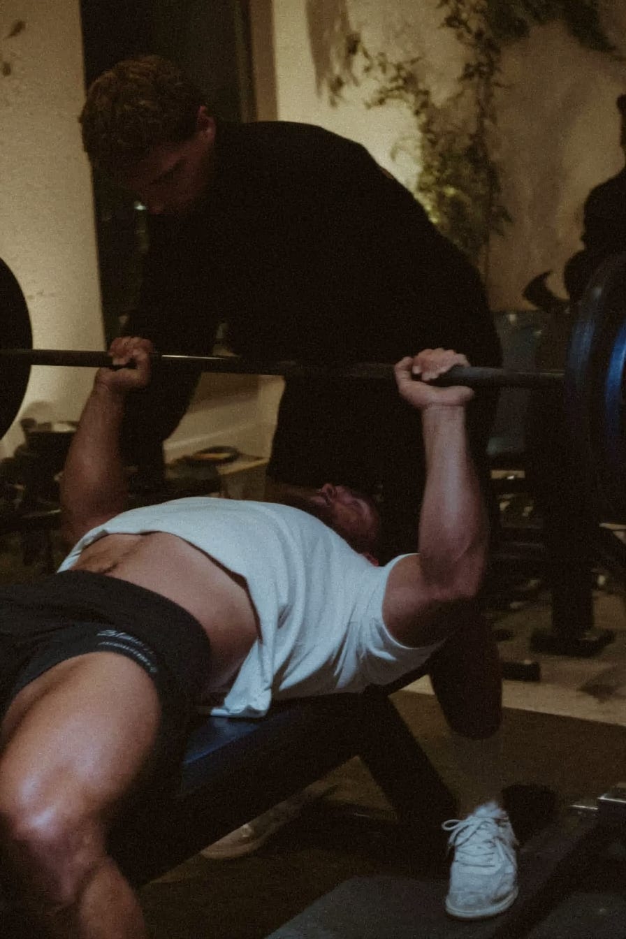 Powerlifter performing a heavy benchpress with a spotter in the gym.
