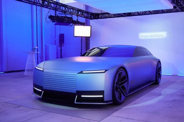 A futuristic car under pinkish-purple light in a white room. On the wall behind it is a sign that says Copy Nothing.