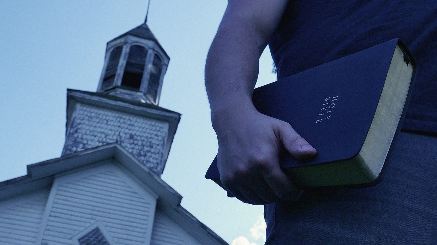 A picture of the right side of the author's mid-section, focusing on a Bible held in his hand at his waist. A white church steeple looms in the backdrop at a crooked angle to the left.